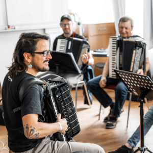 Dozent Alex Almedia der vor Akkordeon- Schülern etwas auf dem Akkordeon vorspielt