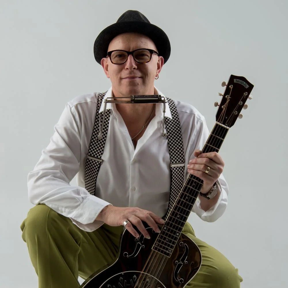Dozent Eddie Martin er trägt ein weißes Hemd und einen Hut, hält eine Gitarre in der Hand
