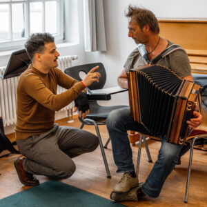 Dozent Jakob Steinkellner der sich beim Akkordeon spielen mir einem Schüler unterhält